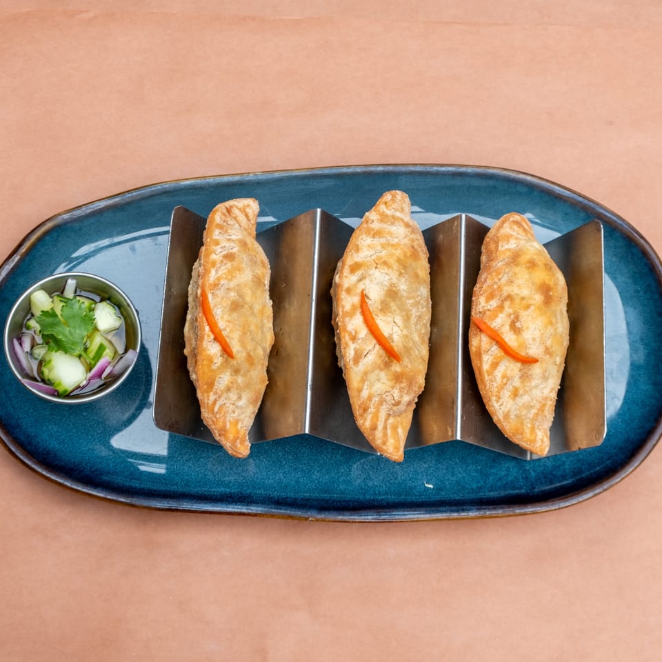 Three golden-brown empanadas with red pepper strips, served with a side of pickled vegetables.