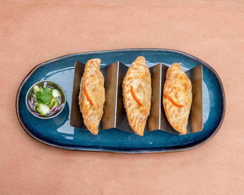 Three golden-brown empanadas with red pepper strips, served with a side of pickled vegetables.