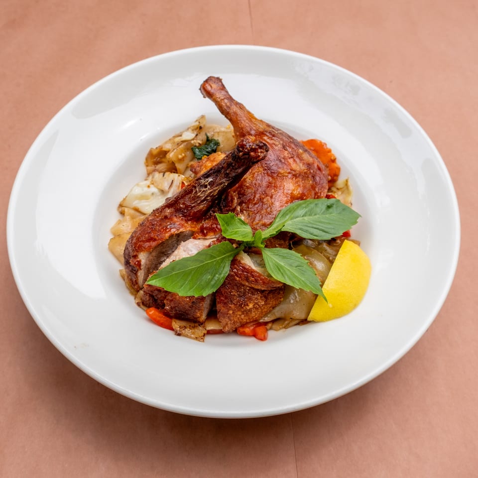 Crispy duck leg and thigh served over noodles and vegetables, garnished with basil and lemon.