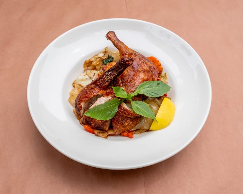 Crispy duck leg and thigh served over noodles and vegetables, garnished with basil and lemon.