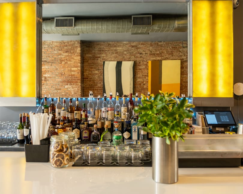A well-stocked bar with various liquor bottles, wine, glasses, and a plant on a white counter.