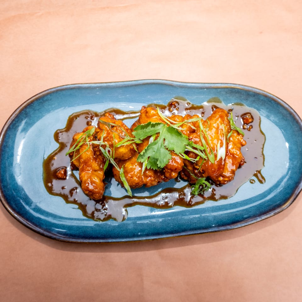 Sweet and sour chicken wings with cilantro and scallions on a blue plate.