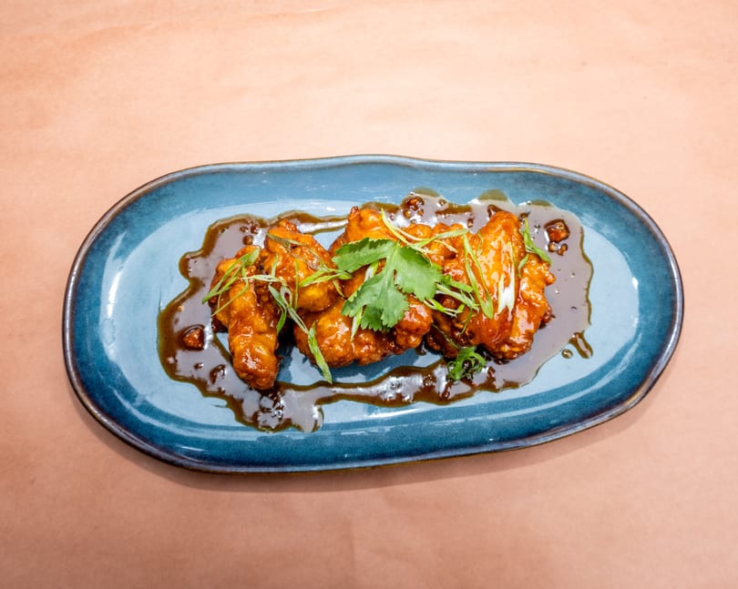 Sweet and sour chicken wings with cilantro and scallions on a blue plate.