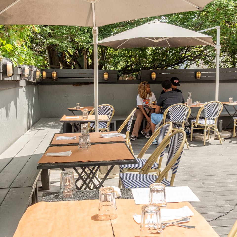 Outdoor patio dining area with tables, chairs, umbrellas, and people enjoying a meal.