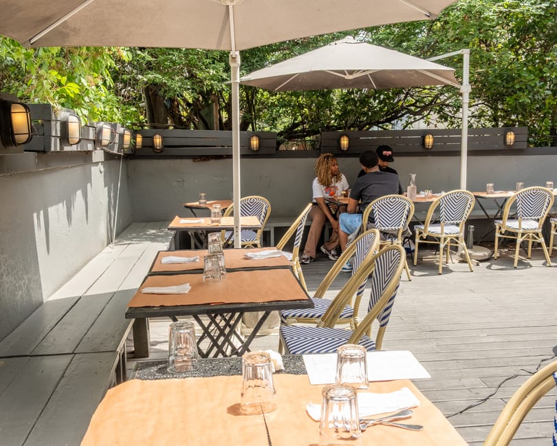 Outdoor patio dining area with tables, chairs, umbrellas, and people enjoying a meal.