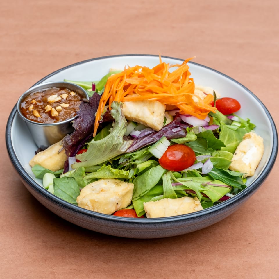 Fresh green salad with fried tofu, cherry tomatoes, shredded carrots, and peanut sauce.