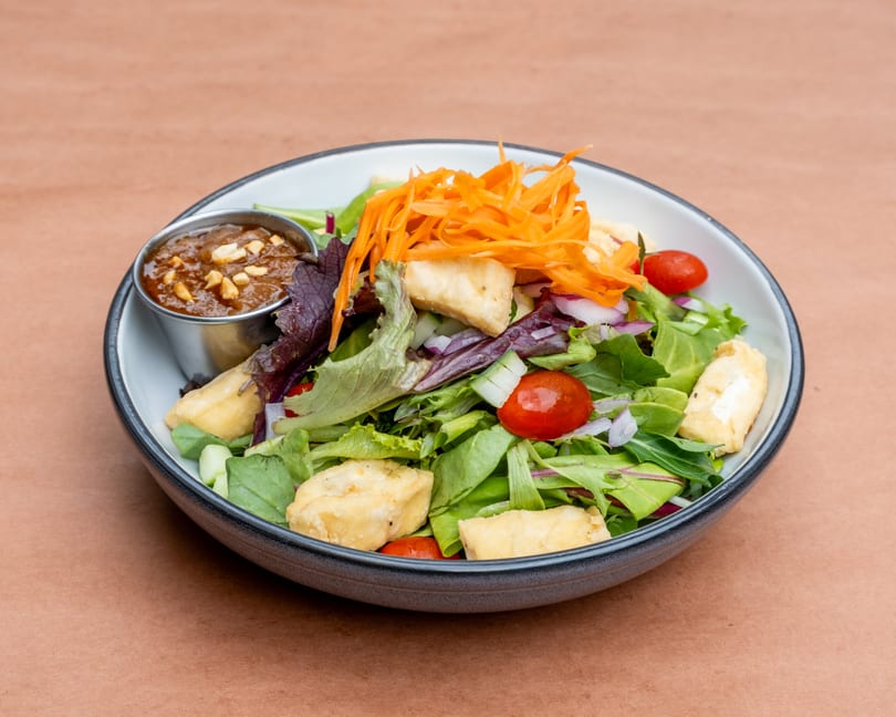 Fresh green salad with fried tofu, cherry tomatoes, shredded carrots, and peanut sauce.