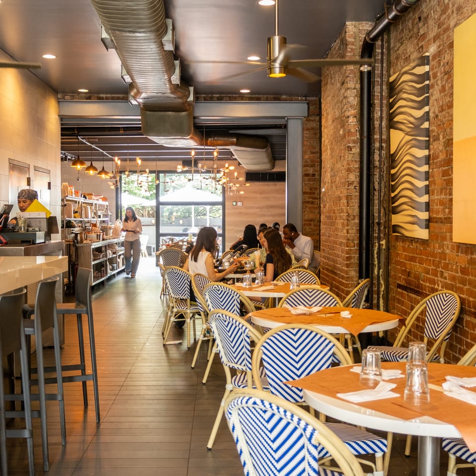 Restaurant interior with patrons dining at tables, a bar with stools, and exposed brick walls.