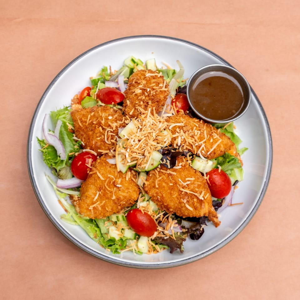 Coconut shrimp salad with mixed greens, cherry tomatoes, red onion, cucumber, and a side of dressing.