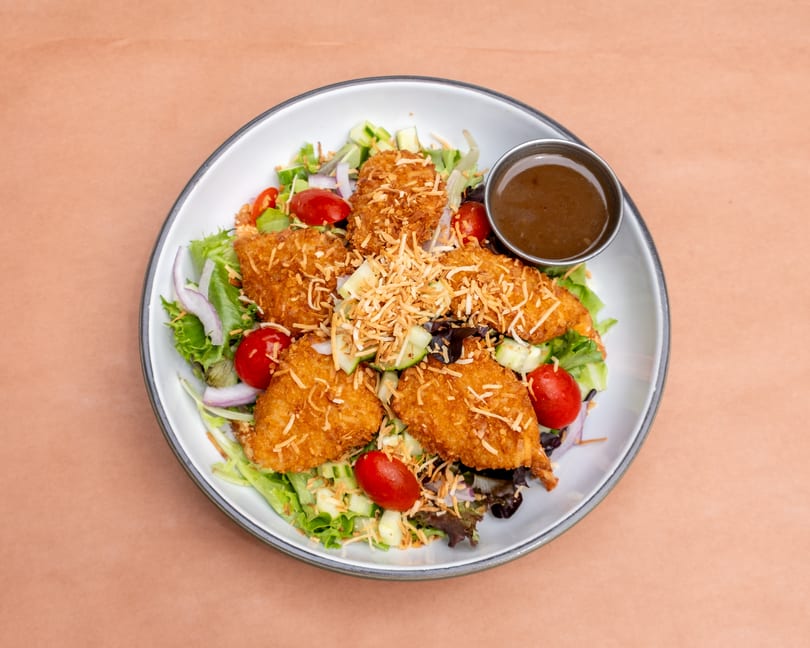 Coconut shrimp salad with mixed greens, cherry tomatoes, red onion, cucumber, and a side of dressing.