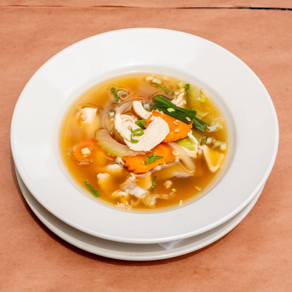 A white bowl of chicken and vegetable soup with carrots, onions, and green onions.
