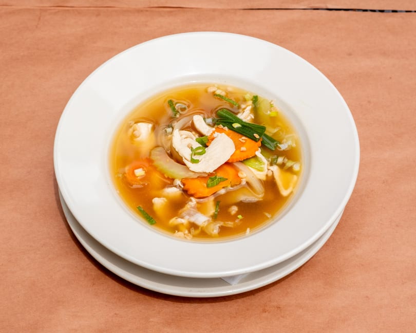 A white bowl of chicken and vegetable soup with carrots, onions, and green onions.