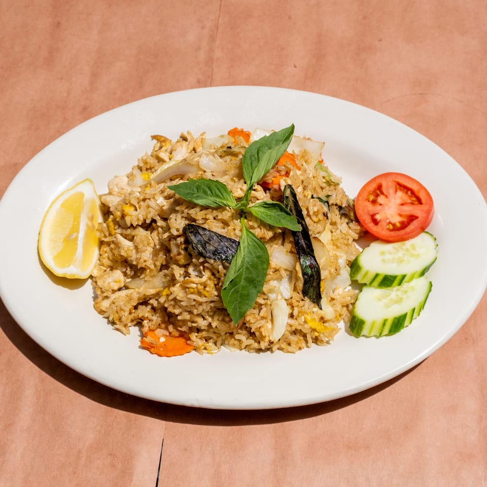 Fried rice with chicken, vegetables, basil, lemon, tomato, and cucumber on a white plate.