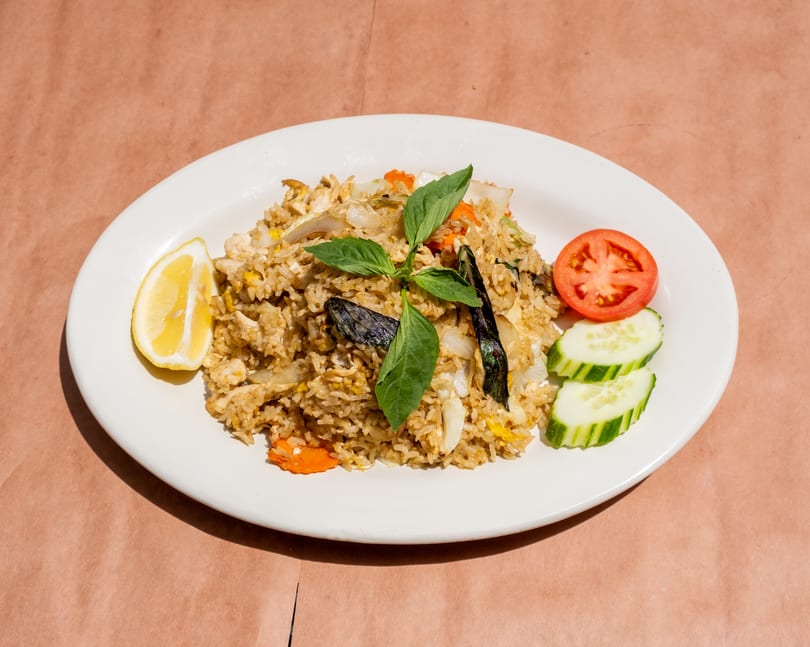 Fried rice with chicken, vegetables, basil, lemon, tomato, and cucumber on a white plate.