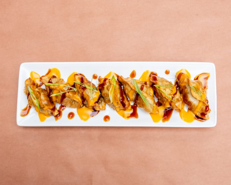 Fried dumplings drizzled with orange and brown sauces, garnished with green onions on a white plate.